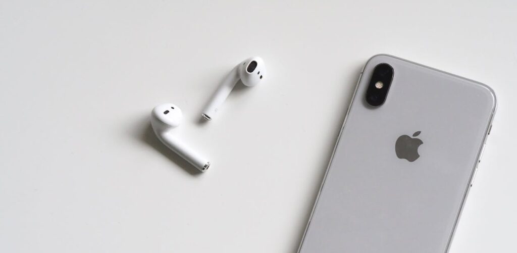 Close-up of a silver iPhone and wireless AirPods on a sleek white background.
